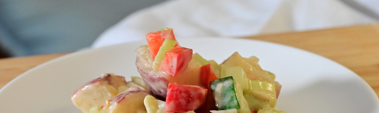 Brightly colored potato salad on a white plate on a bamboo cutting board