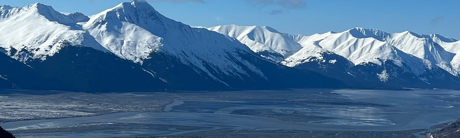 View from on top of a mountain looking out over an inlet and more snowy mountains.