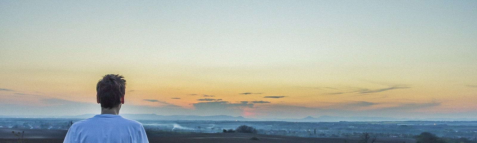 A guy sitting and facing mountains afar.