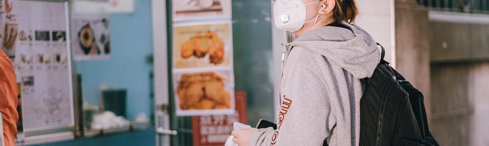 An Asian American woman with a mask standing in line at a restaurant