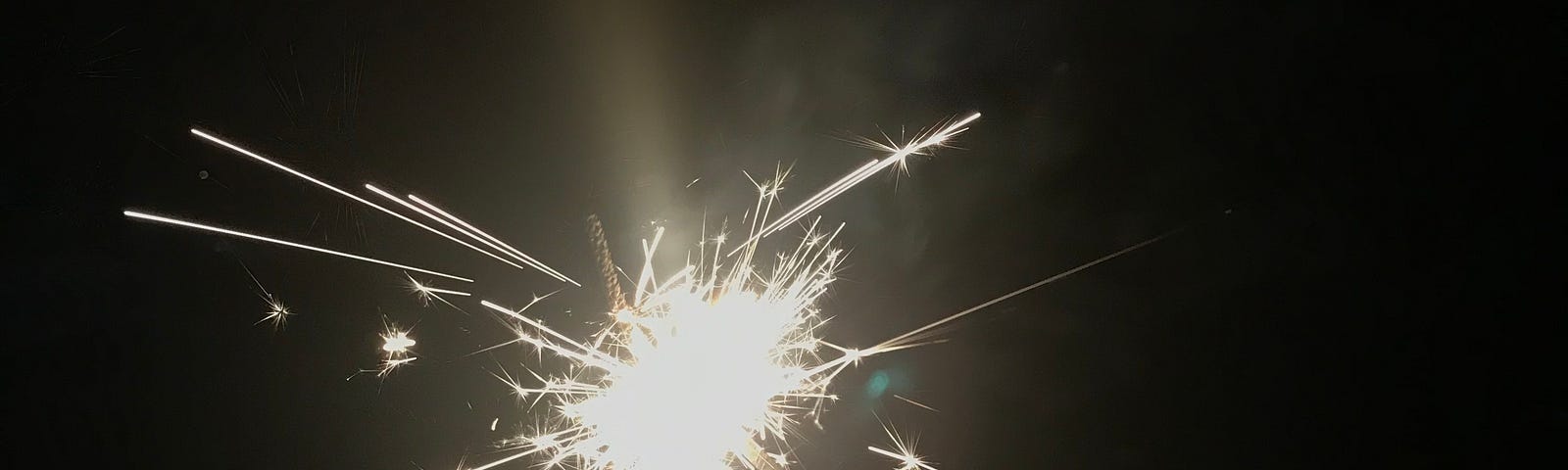 A hand holds a sparkler firecracker as it spits small flames of light into the darkness.