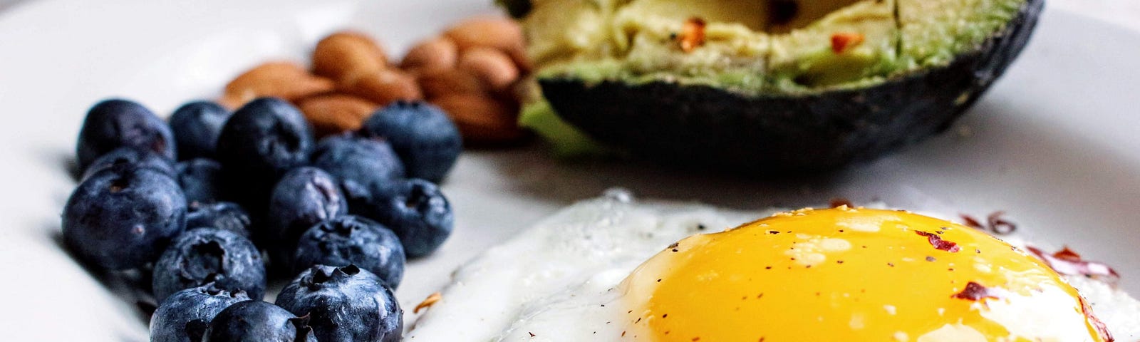 Fried egg, avocado, almonds and blueberries on plate