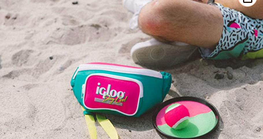 a beach with a neon multi colored fanny pack. The fanny pack says igloo: Stay Cool in a 1990s font. There is a velcro ball set next to the fanny pack. A person in 1990s patterned shorts is sitting next to the fanny pack.