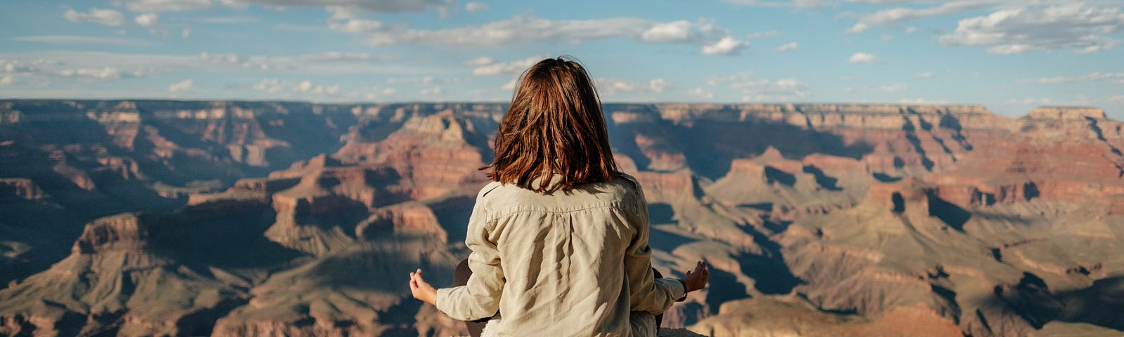 Long-haired person sitting facing a natural view with their back to the camera, in a meditative position.