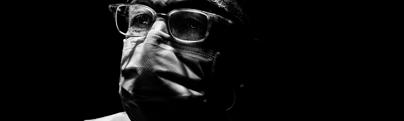 Shadowy black and white picture of a medical professional in a mask and glasses.