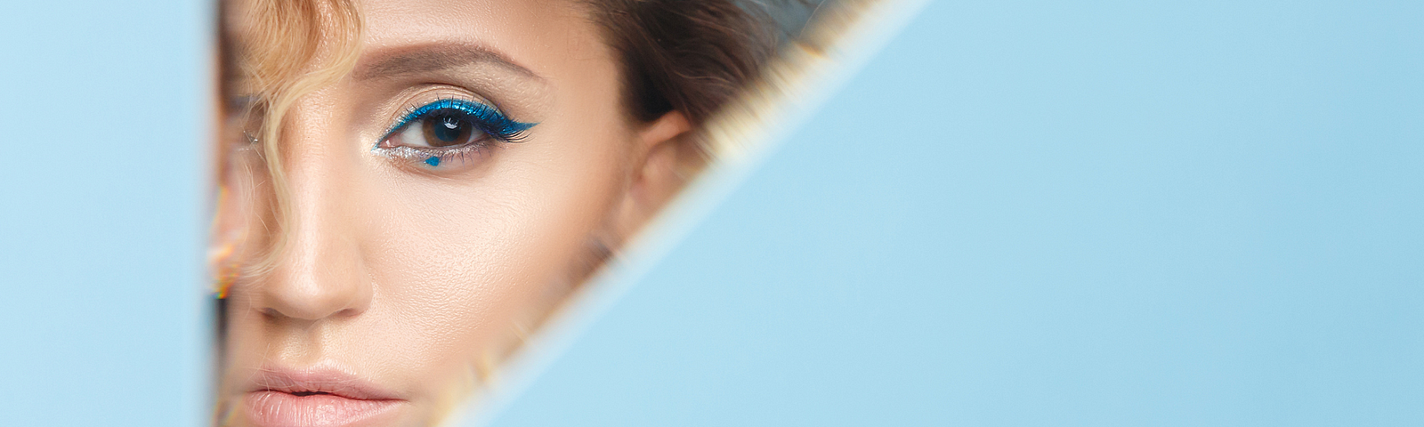 light blue background with a triangular mirror on left and the reflection of a woman with blue eyeshadow. Words in bottom right: I deserve to feel good about the person I see in the mirror.