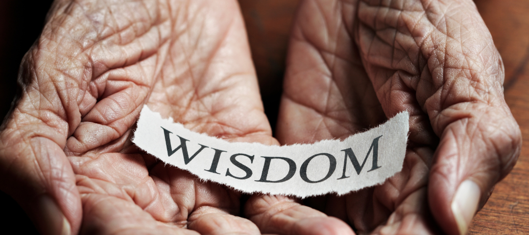 Wrinkled hands holding a paper that says ‘wisdom’