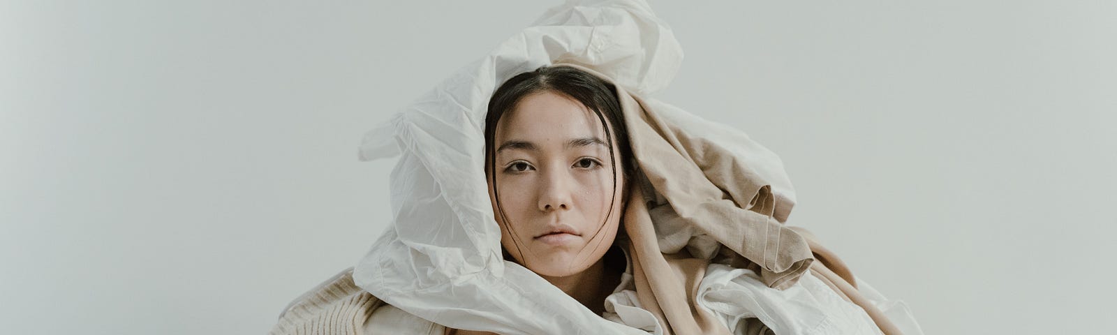 Image of a tired looking Asian woman with a big pile of clothes strewn all over her