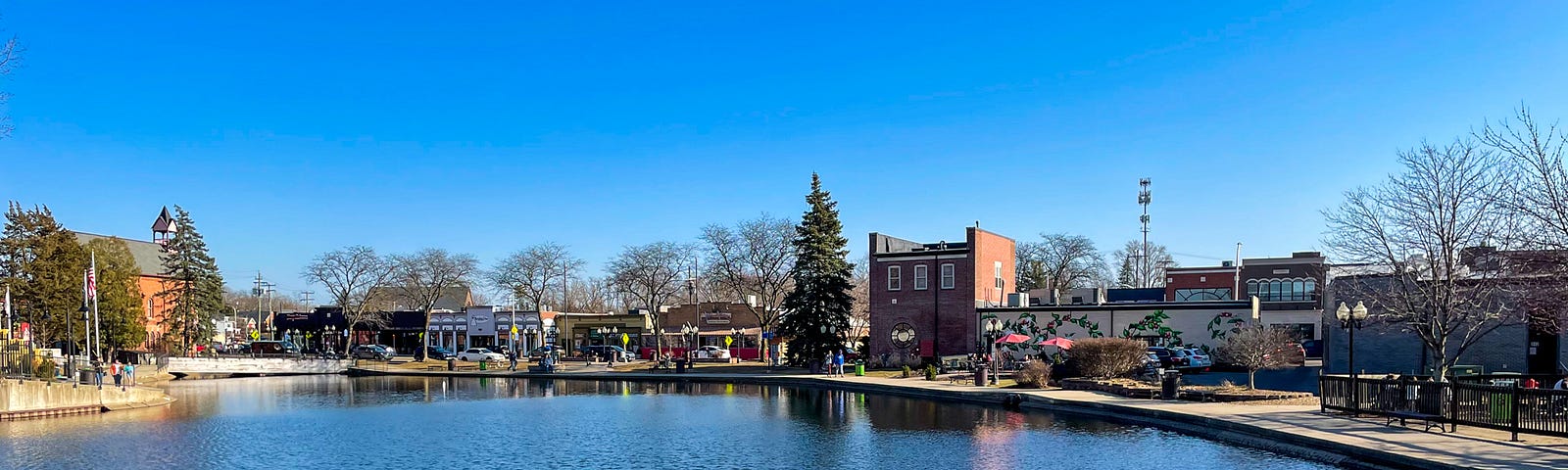 Across a millpond there is a street of buildings and trees.