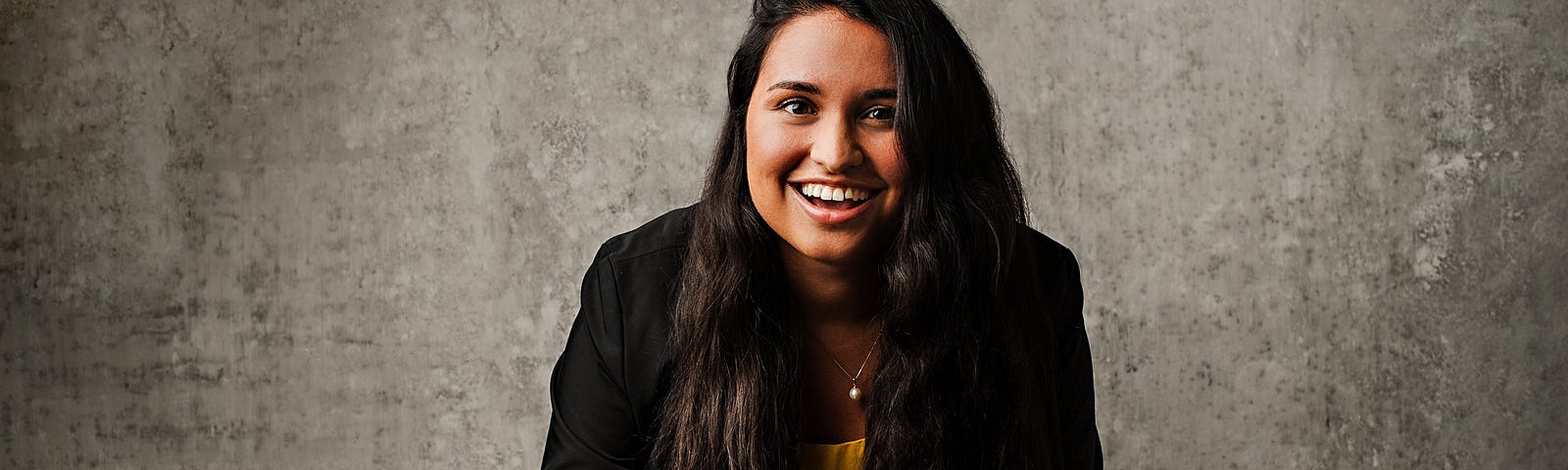 Headshot of Vanessa in yellow shirt with black blazer at a wooden table