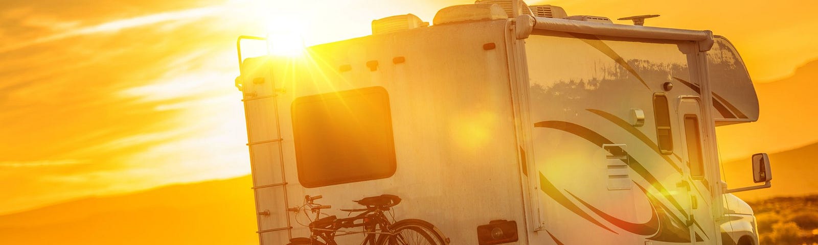 Photo of an RV driving on highway with the rising sun ahead at the far side of the horizon.