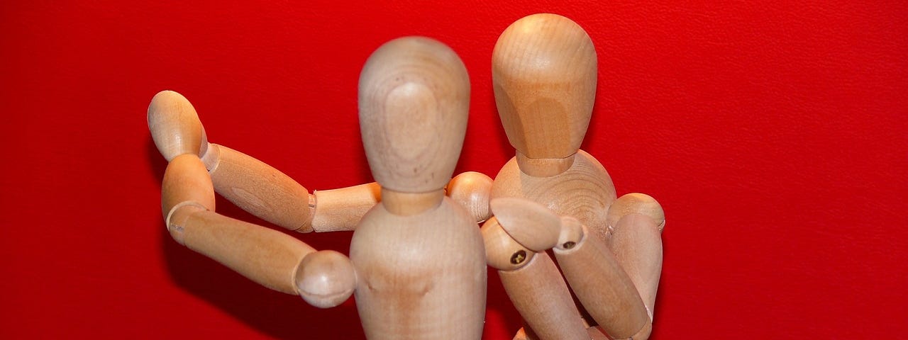 Two wooden dolls dance together before a red wall