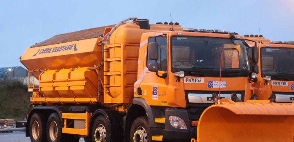 A large orange winter service vehicle, with snow plough attachment in front. On the side its name is show as Carrie Bradthaw