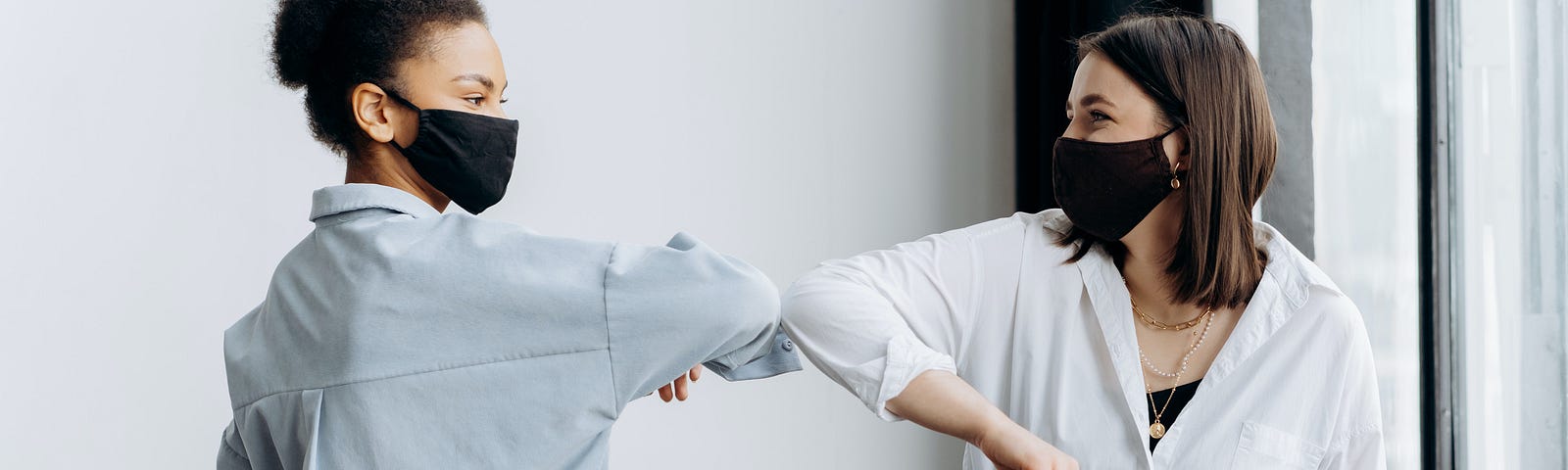 Two masked women bumping elbows