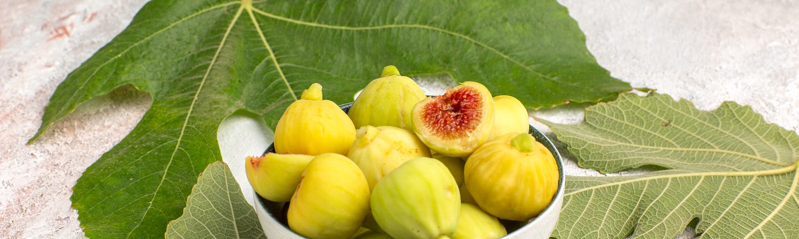 Fig fruit in a bowl surrounded by fig leaves