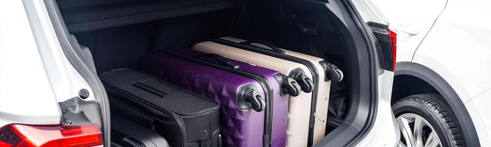 The back hatch of a car is open, revealing four suitcases nestled in to the back area.