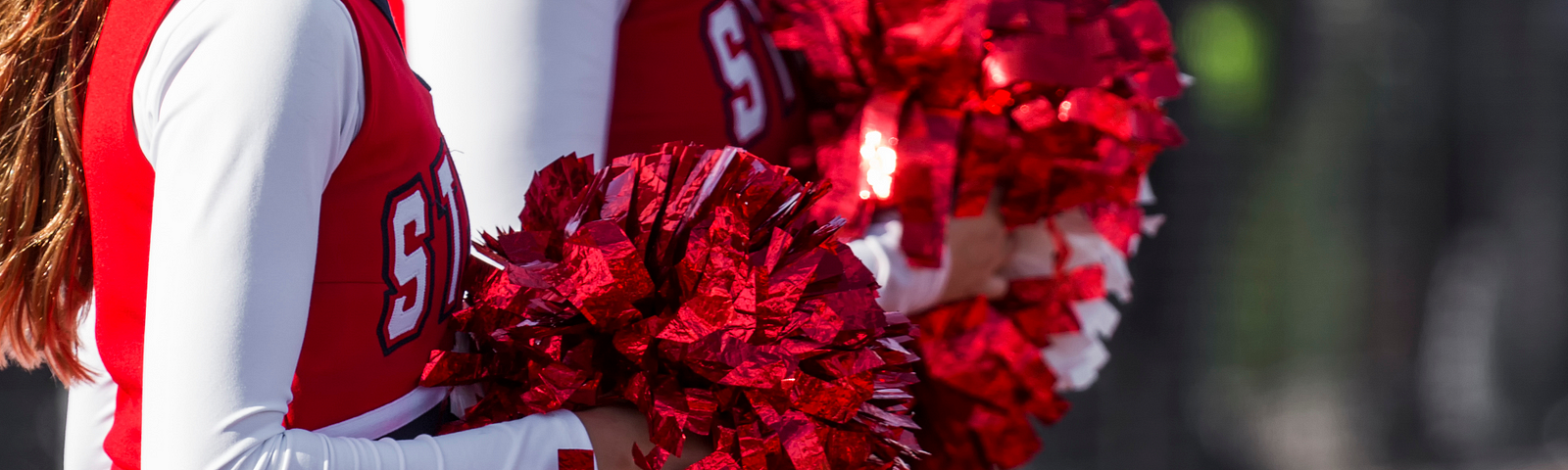 Close up photo of two cheerleaders dressed in red holding red and white pom-poms.