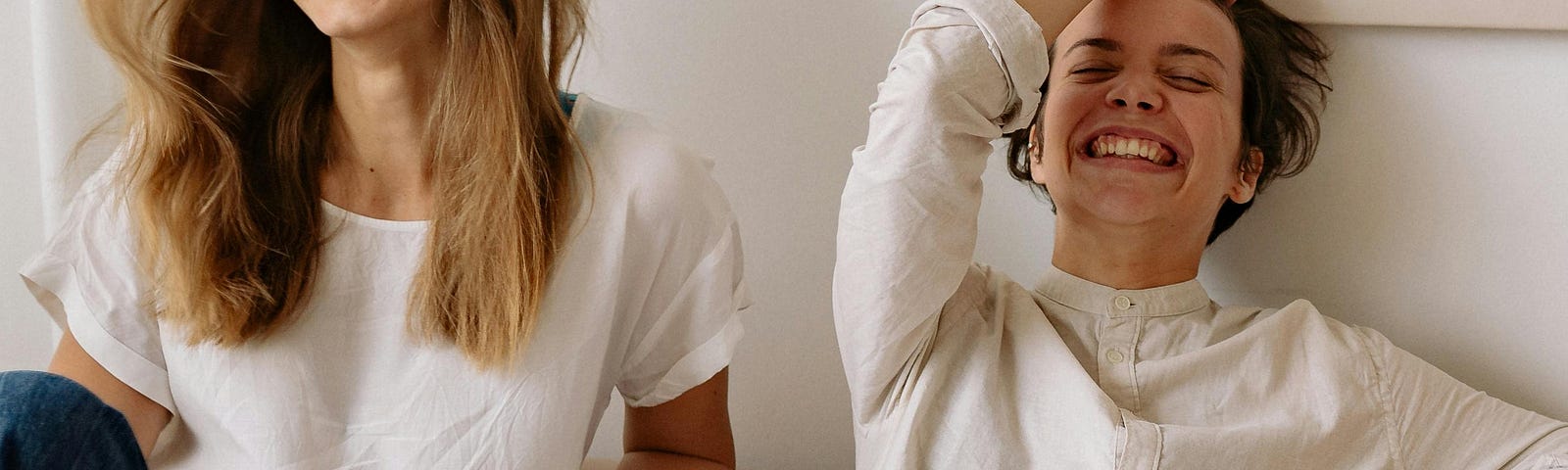 Woman in white crew neck t-shirt sitting beside woman in white long sleeve shirt laughing