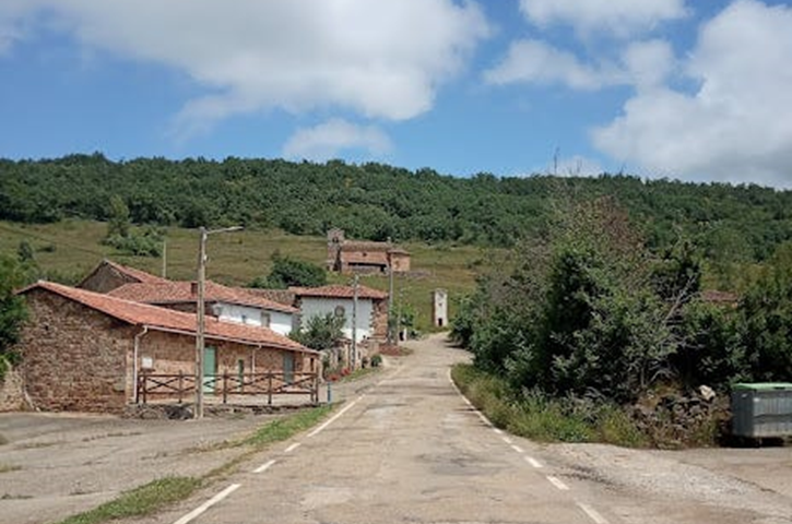 The entrance road to the village of Villanueva de la Torre. Some houses on the left and the church at the end, on a hill surrounded by a green landscape