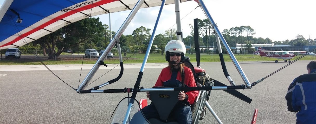 The author is dressed in a jumpsuit, wearing a helmet, and sitting in a hang glider.