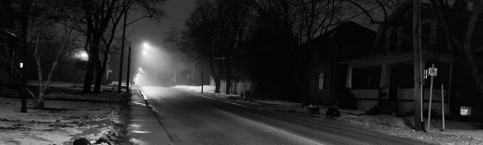 Dark street, with some fog, and a street light burning at the end
