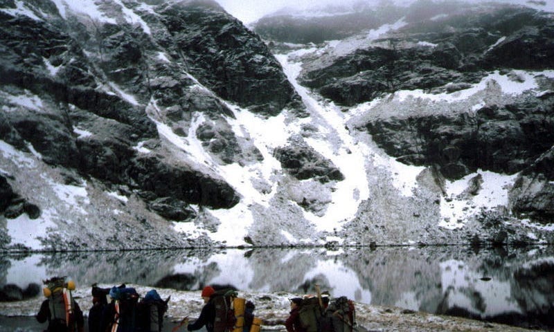 Several equipped climbers beside a body of water at the foot of snow-covered hills