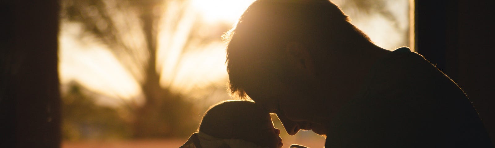 Outline of a man holding a baby close, backlit against the sun