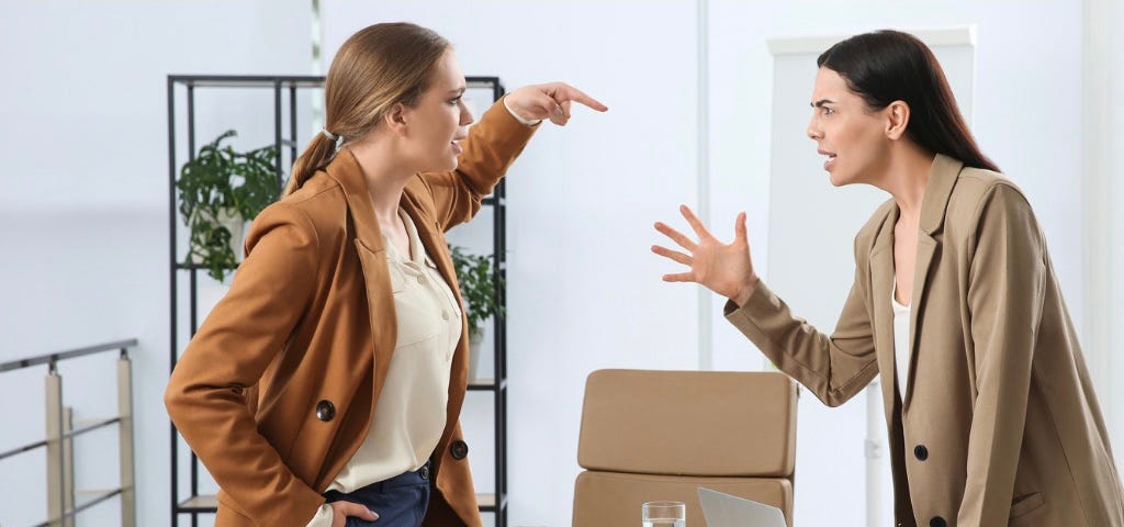 Two women standing on oppos sides of a desk in conflict with each other.