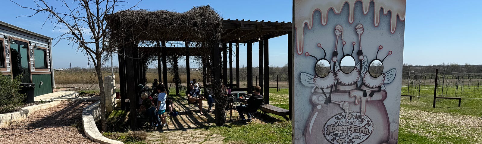 A photo prop stand with three bees sits in front of a pergola at Walker Honey Farm.