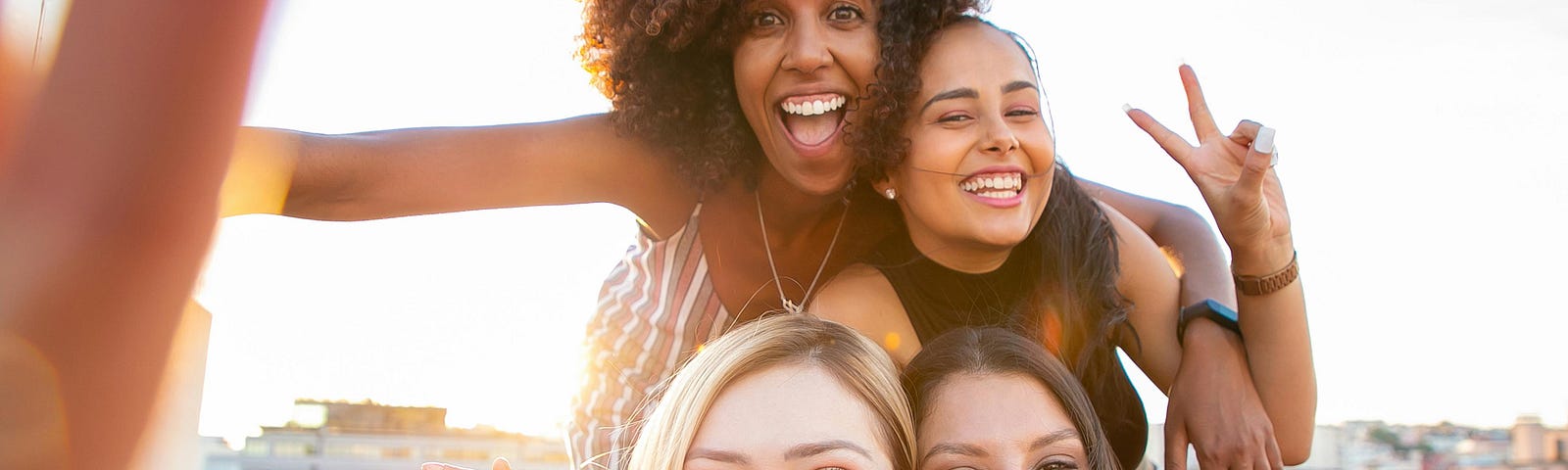 Cheerful young diverse women showing V sign while taking selfie on rooftop