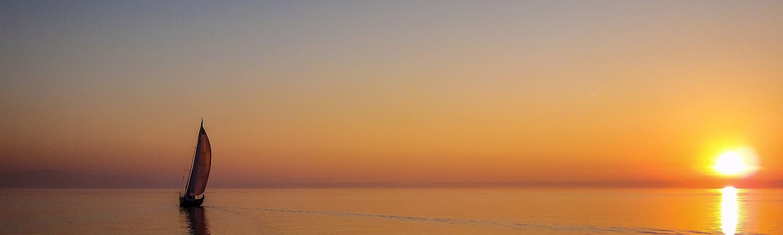 Barco velejando em alto mar em sentido ao por do sol