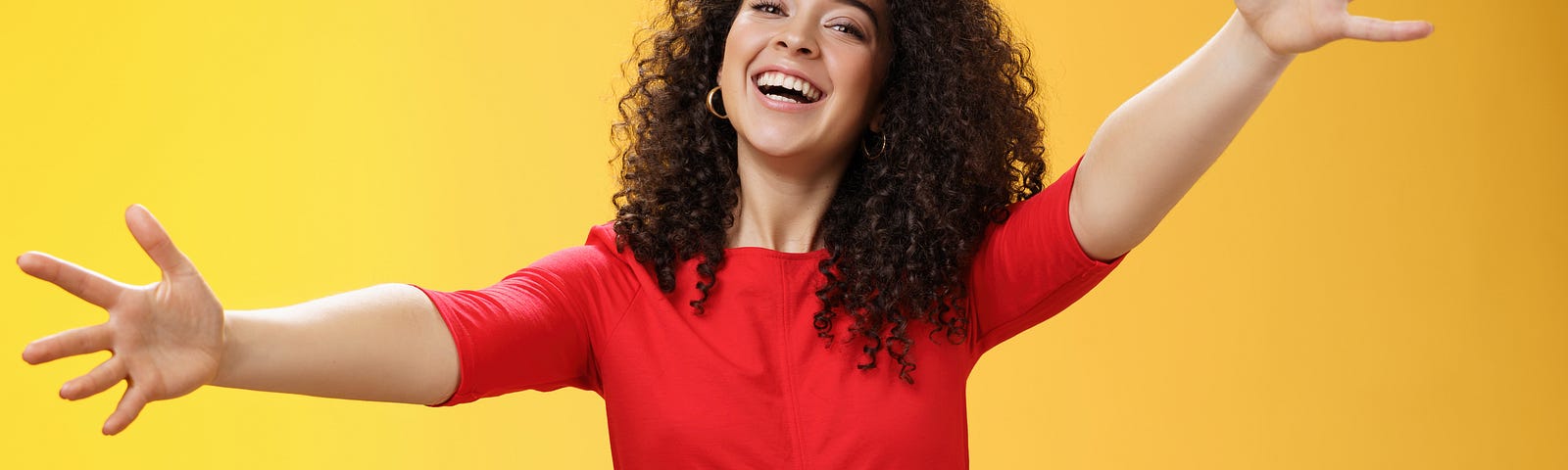Come into my arms. portrait of friendly and loving, caring charming woman with curly hair in red casual dress spread hands as wanting give hug smiling broadly at camera giving warm