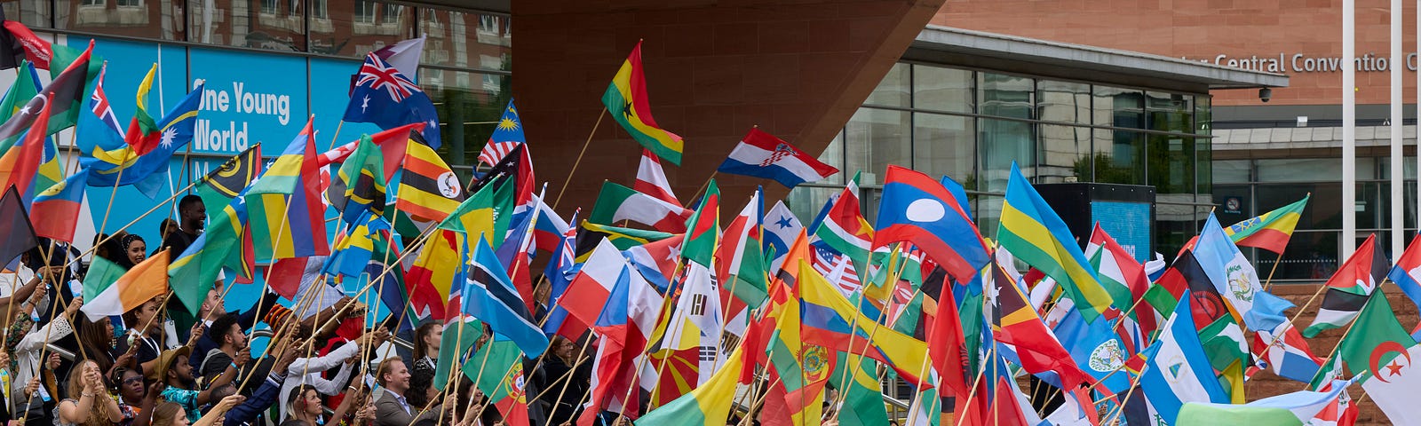 A large group of young leaders stand in a group waving flags from countries around the world.