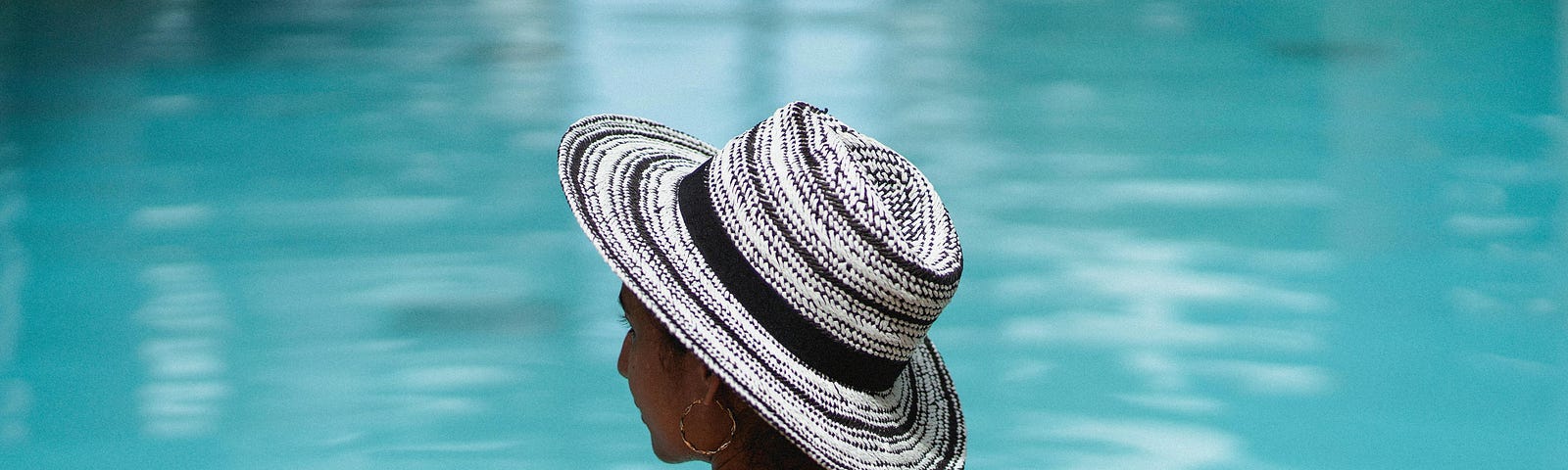 Back view of a lady resting with her arms at the edge of a pool, looking left. Photo by Armin Rimoldi on Pexels.
