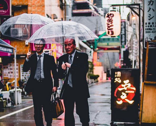 2 businessmen in Japan (?) walking under transparent umbrellas