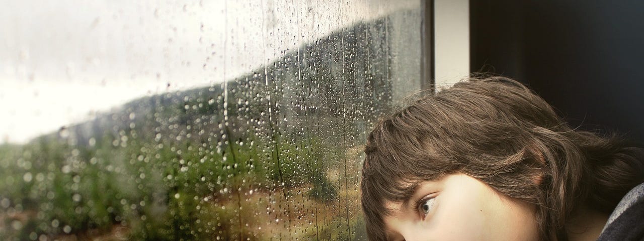 A young boy looking wistfully out a window.
