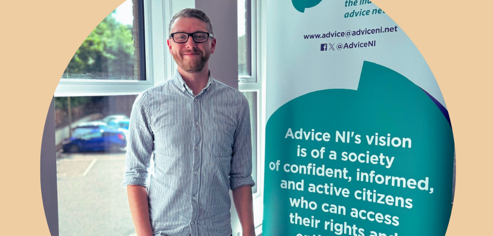 Alsdair from Advice NI standing next to a pop-up banner of Advice NI