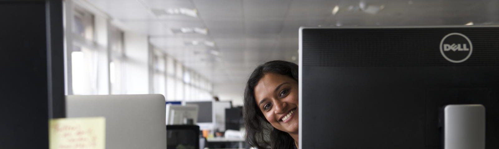 Peson peering from behind a desktop, smiling