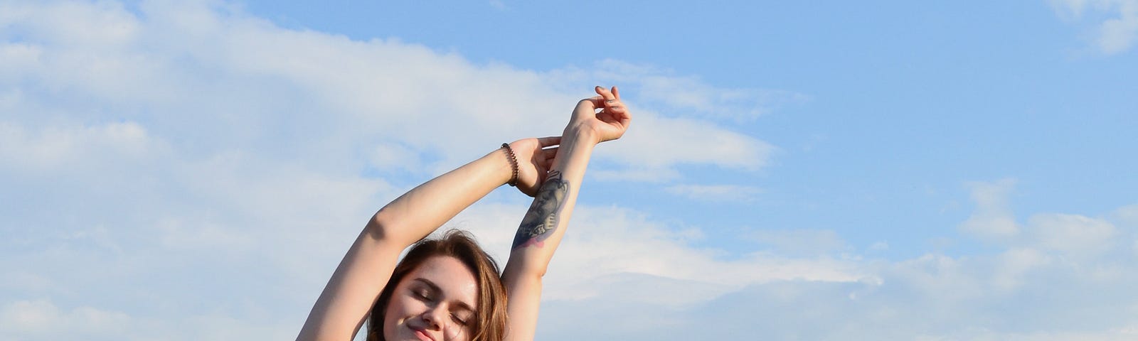 A woman stretches to the sky on a sunny, blue skied day