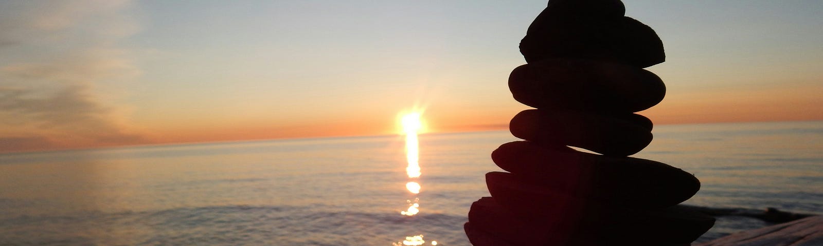 Flat stones in a cairn-like shape, silhouetted as the setting sun sets over the water.