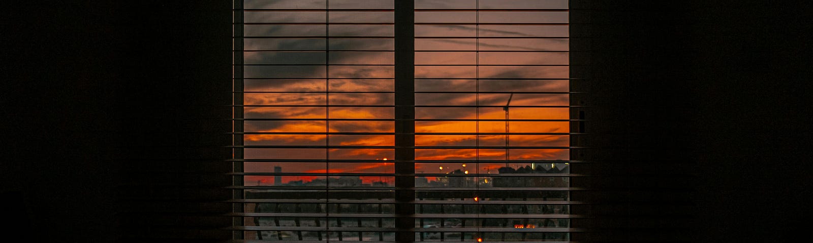 Crumpled blanket in dark room at sunset. The city and the orange sky can be seen through the blinds on the window.