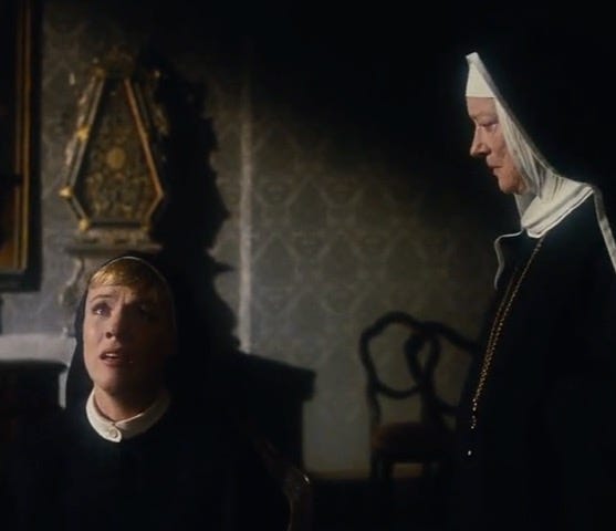 Two nuns. Julie Andrews plays Maria, who is on her knees, gazing into the distance with a distressed look on her face. Peggy Wood plays the Reverend Mother, who is standing above Maria, frowning menacingly.