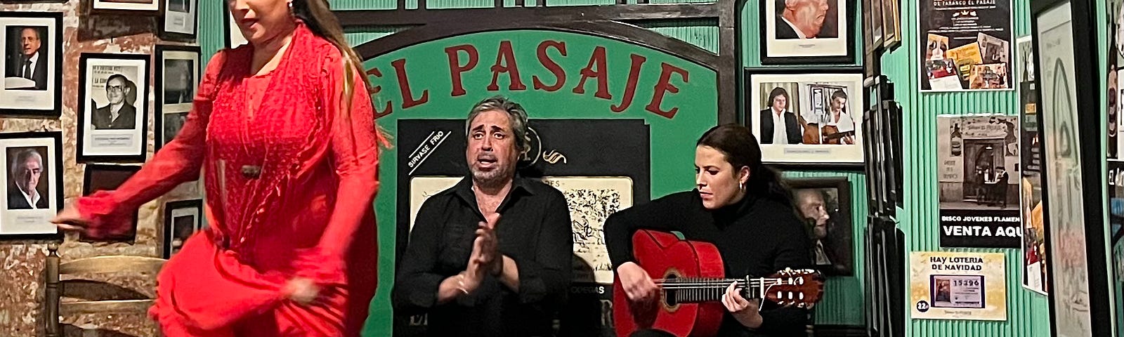 A flamenco dancer in a red dress dancing on stage with a singer and guitarrist behind her