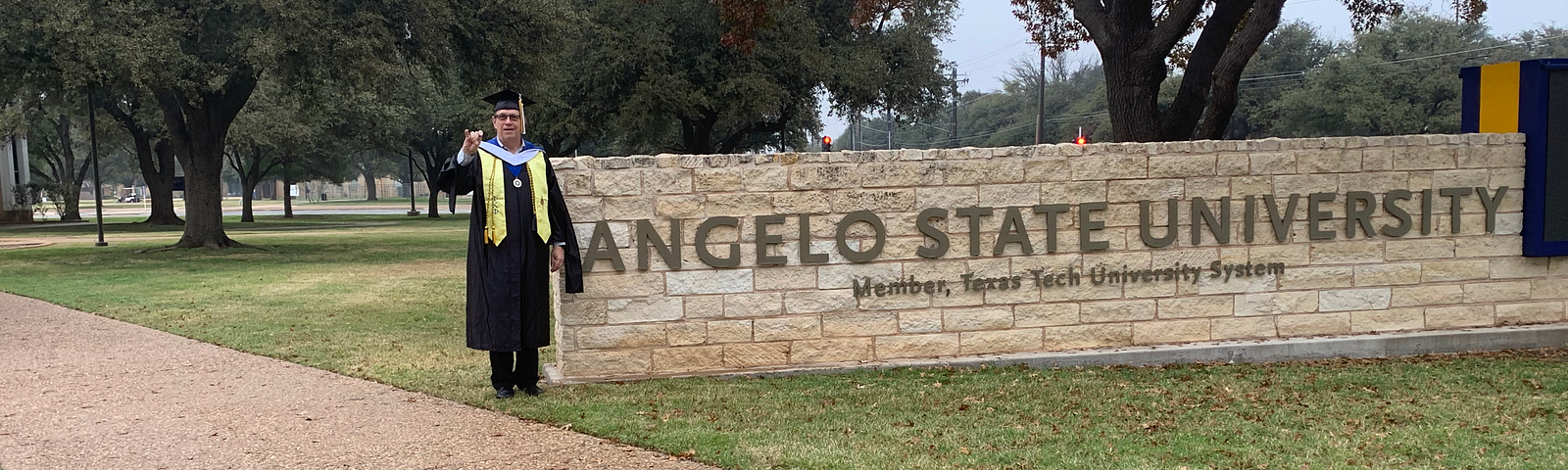 a graduate standing next to a university sign