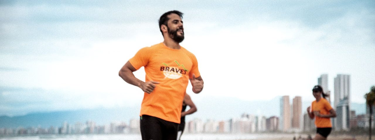 Foto do Thiago em movimento, correndo. Ele veste uma camisa laranja com o nome da equipe estampado.