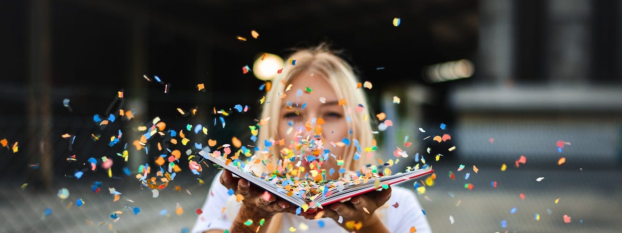 Woman blowing confetti off the pages of an open book.