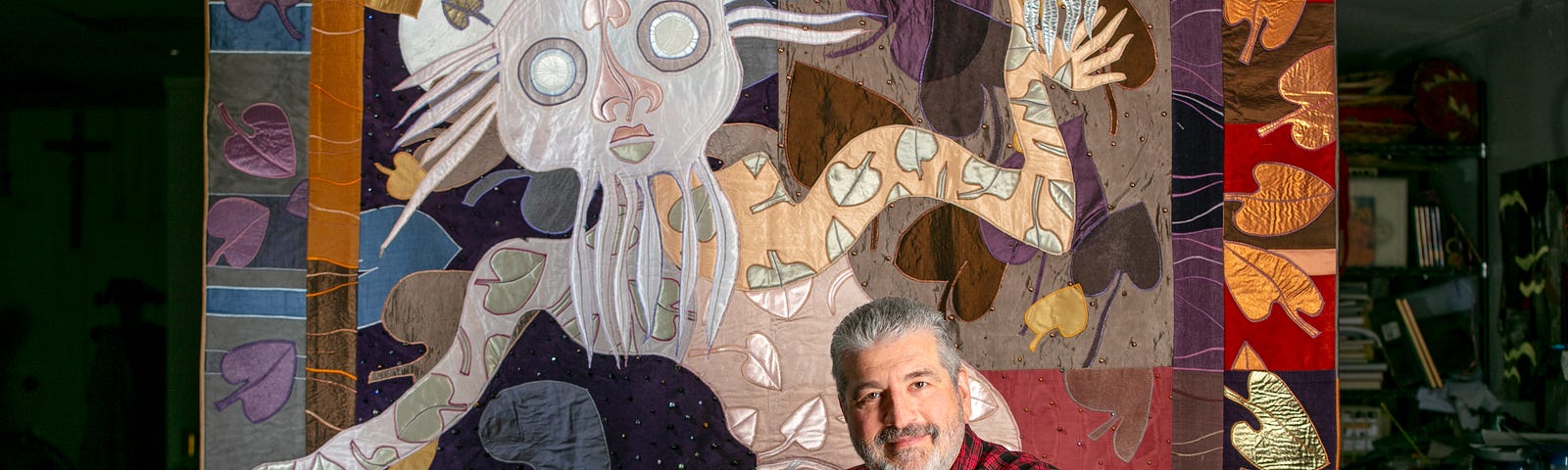 Ken Phillips poses in front of his colorful quilt of Prospero