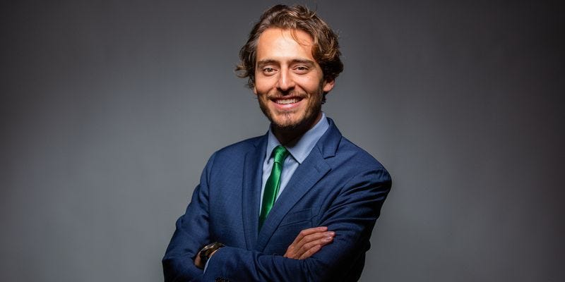 Man in a business suit with a trim beard smiles at the camera.