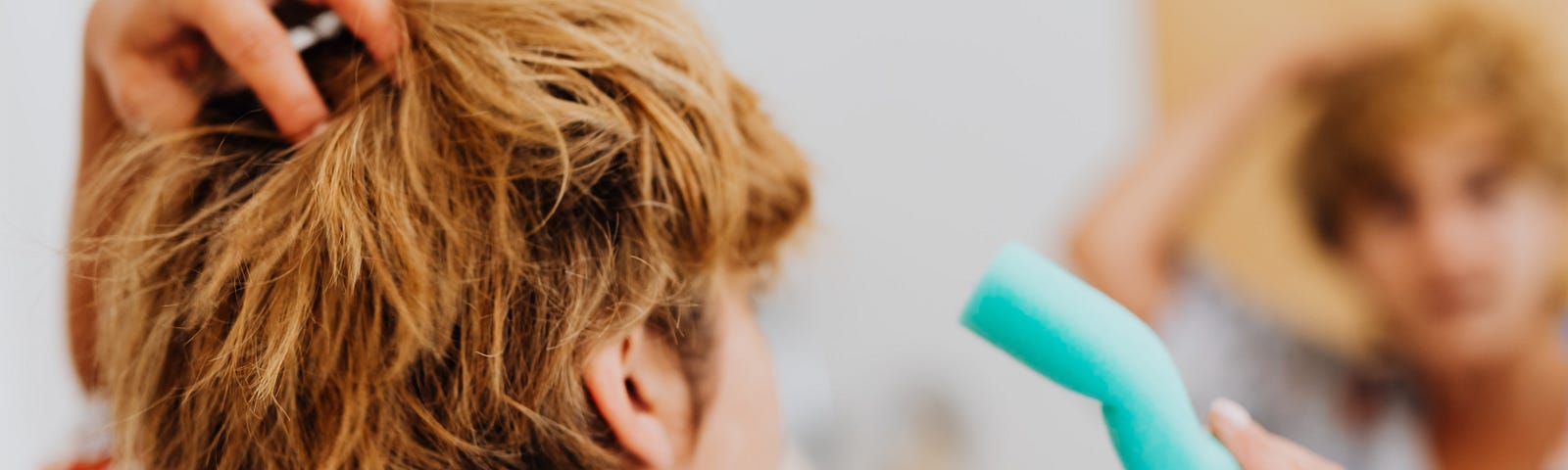 Woman looking in mirror holding hair curlers