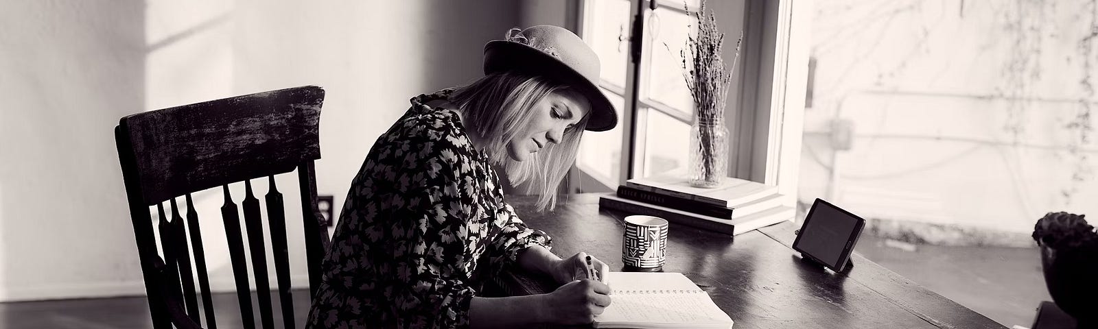 Black and white photo of woman sitting alone at table writing